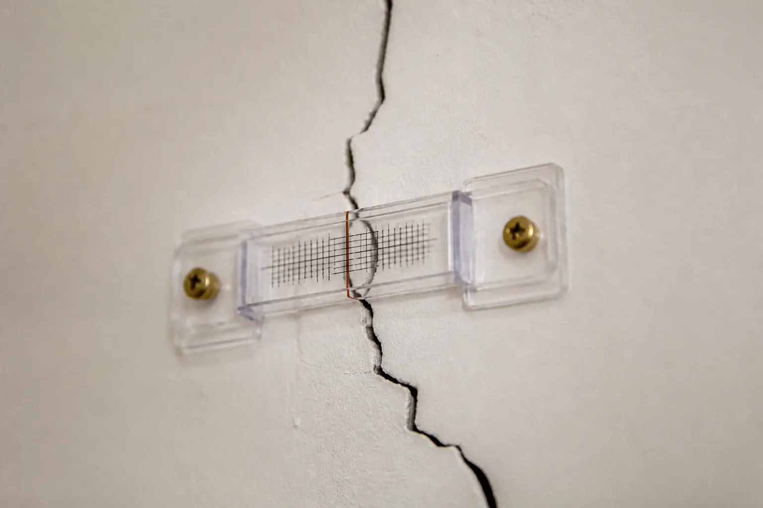Gros plan sur un fissurometre pose sur une fissure de mur interieur